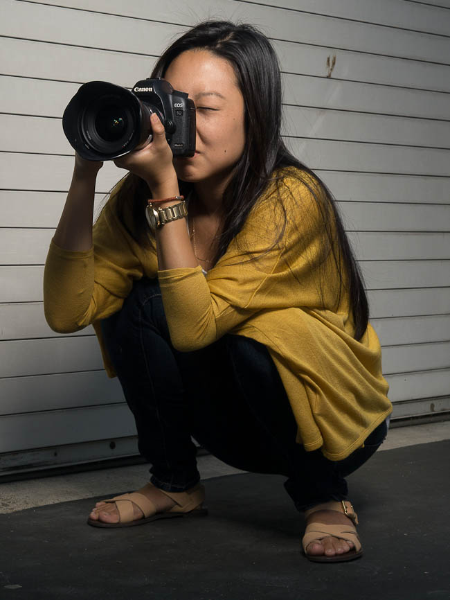 Correct flat-footed squat position with elbows braced on knees demonstrating the super squat camera holding technique for low angle photography